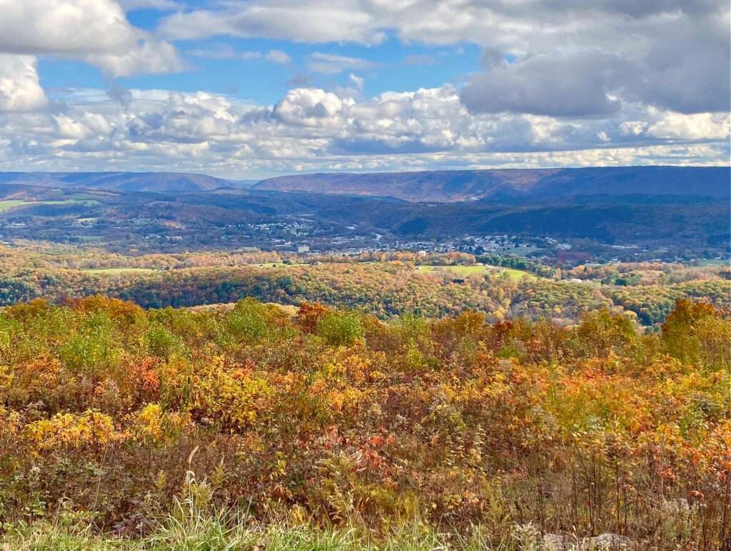 Autumn view across a Pennsylvania valley with colorful trees, distant mountains, and a wide blue sky filled with clouds.